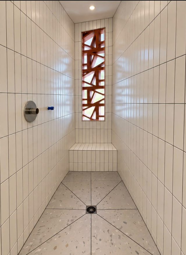Douche de plain-pied après les travaux : carreaux blancs verticaux, banc carrelé, sol aspect terrazzo en pente vers une bonde centrale