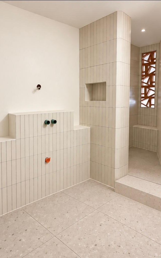 Salle de bain après les travaux : muret et entrée de douche en carreaux blancs verticaux, niche carrelée, sol aspect terrazzo