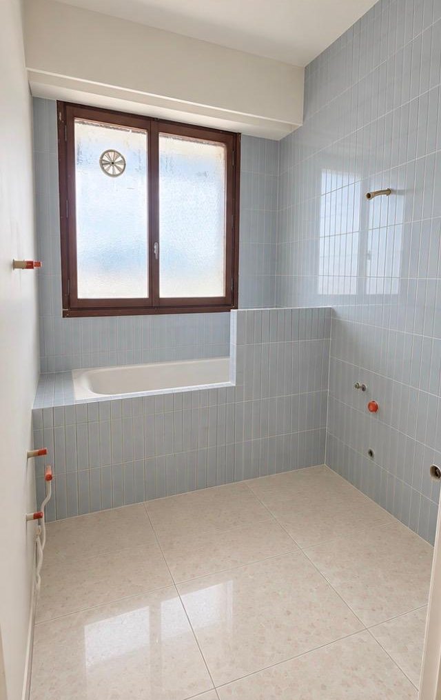 Salle de bain après les travaux : faïence bleue en carreaux verticaux, baignoire avec tablier carrelé, sol aspect terrazzo
