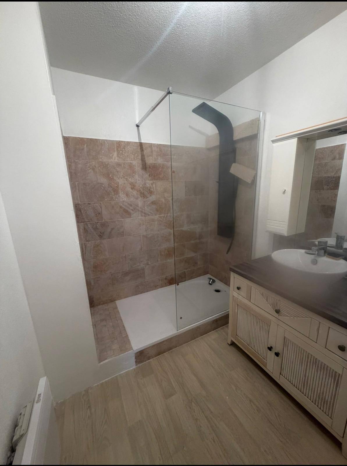 Douche avec paroi en verre et carrelage mural beige aspect pierre, sol aspect bois
