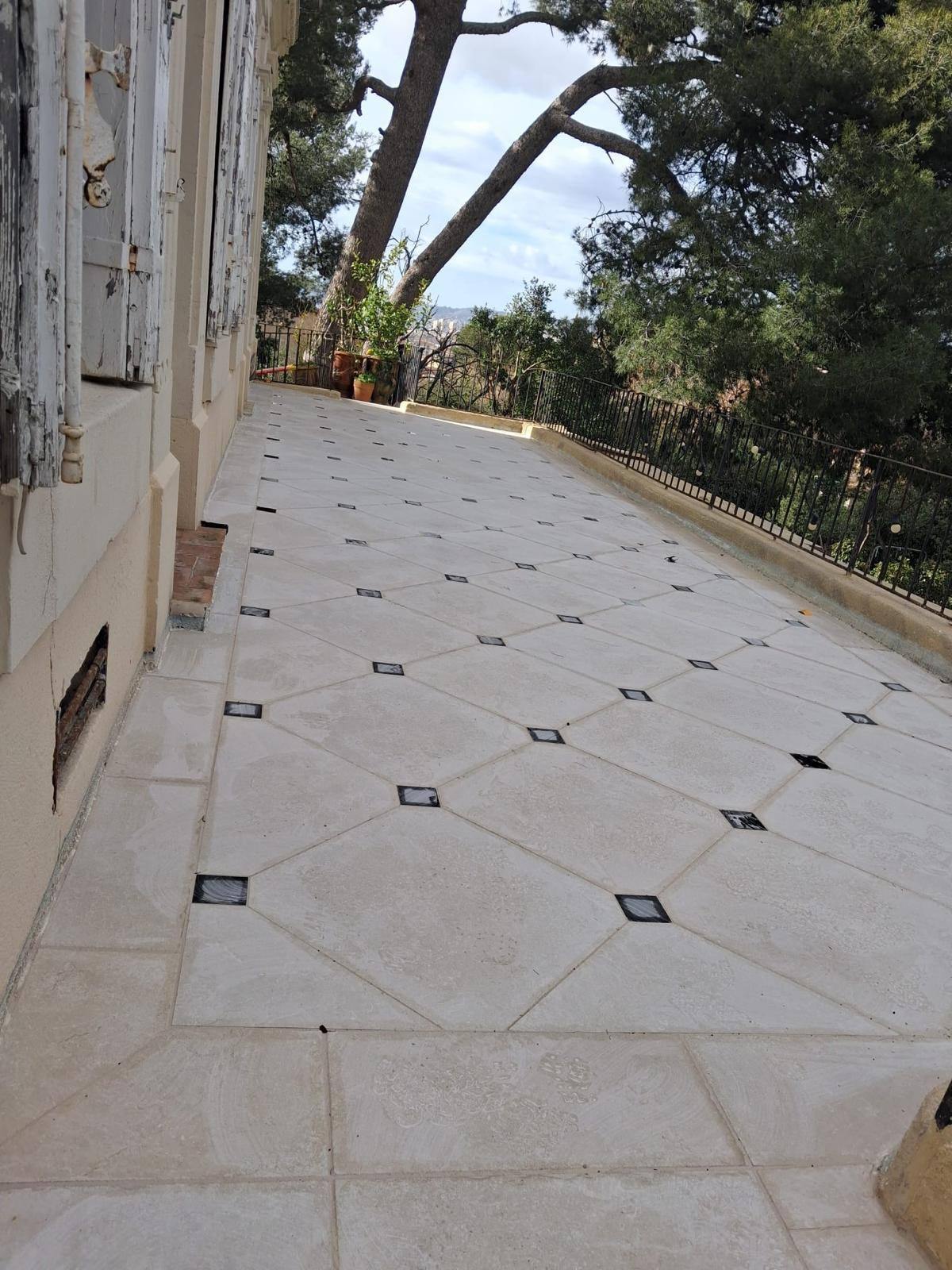 Terrasse en dalles claires à pans coupés et cabochons noirs, garde-corps en fer forgé